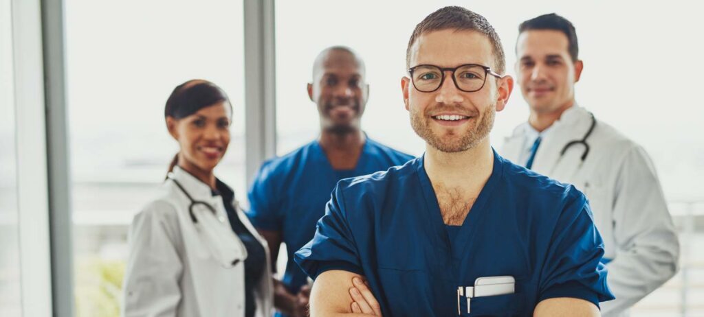 Joven doctor sonriendo a la cámara con tres doctores detrás de é