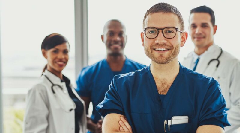 Joven doctor sonriendo a la cámara con tres doctores detrás de é