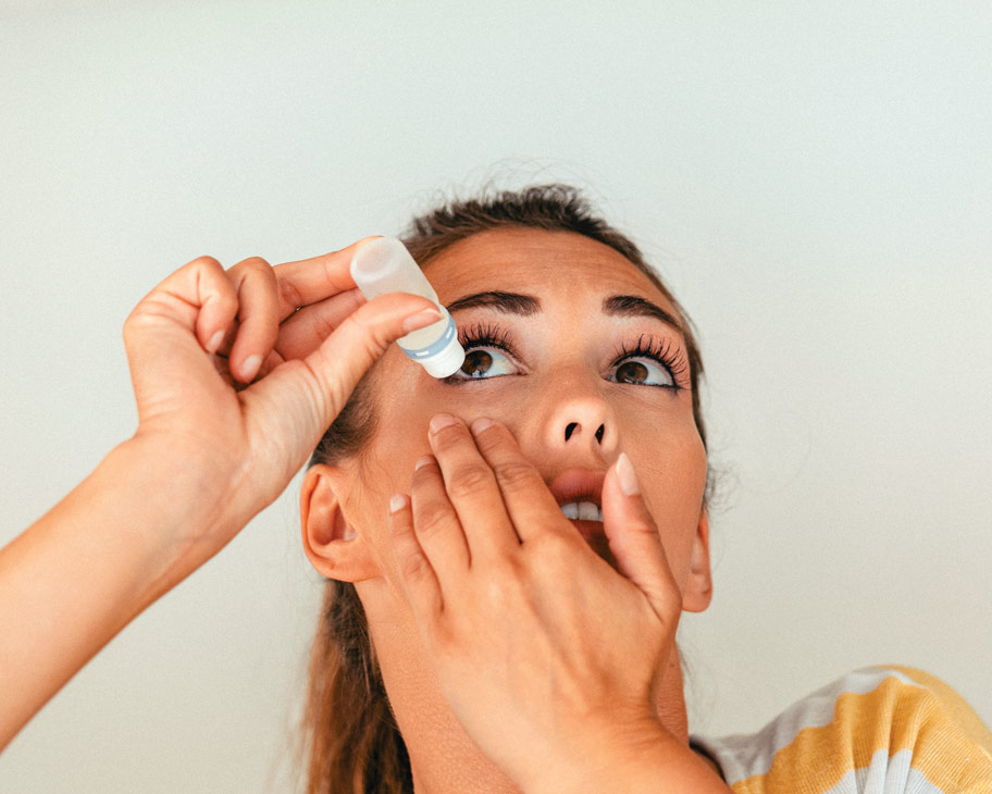 Mujer joven aplicando gotas para los ojos en su ojo derecho