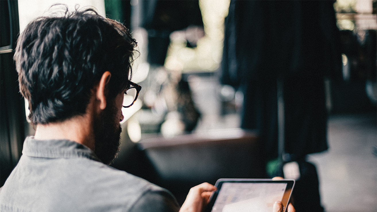 Hombre joven con lentes, de espaldas, leyendo algo en su tableta electrónica