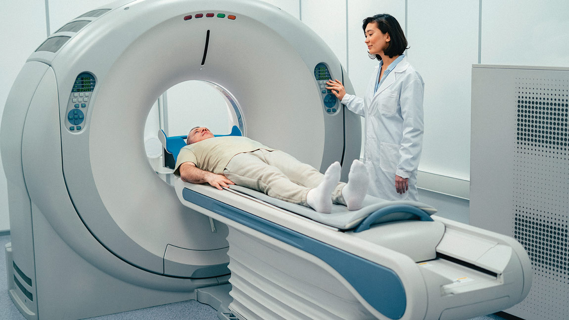 Paciente recibiendo una tomografía, mientras una doctora joven está a su lado utilizando el equipo médico