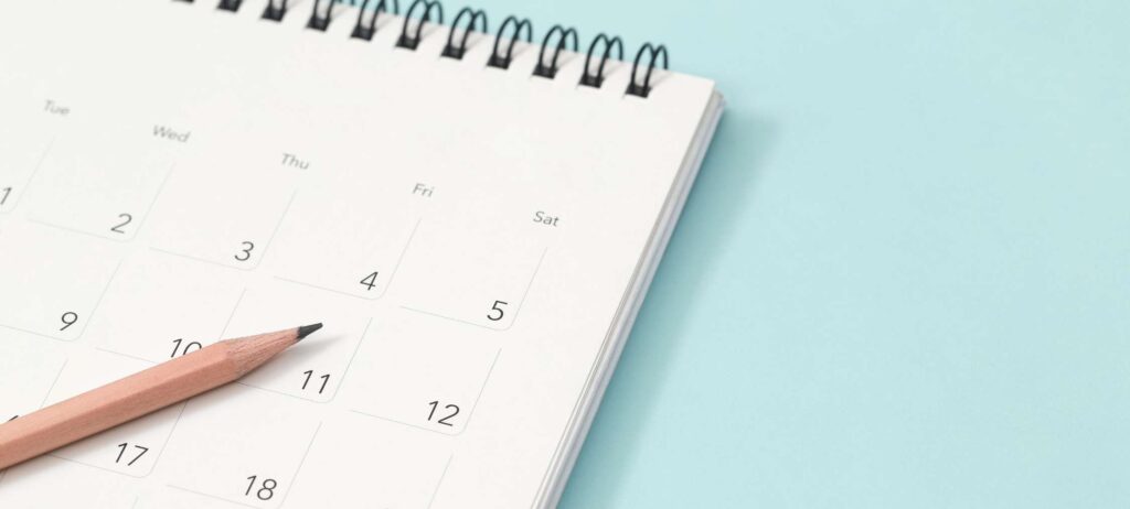 Fotografía de un calendario, con un lápiz sobre él, sobre una superficie color azul claro