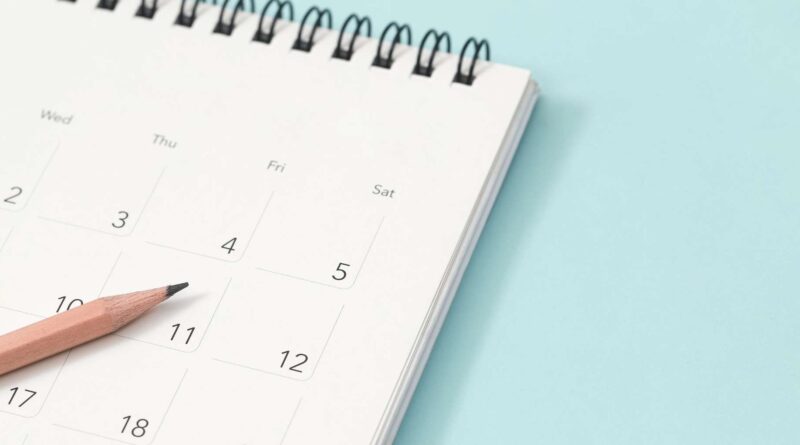 Fotografía de un calendario, con un lápiz sobre él, sobre una superficie color azul claro