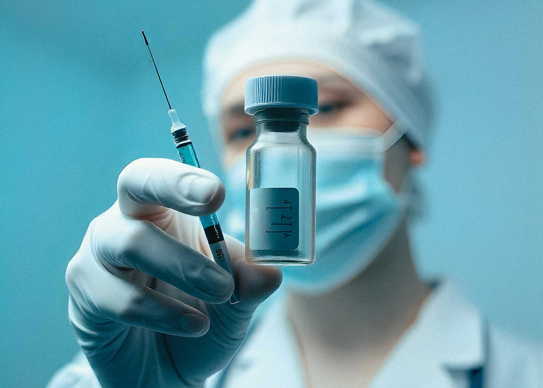 Doctora usando cubrebocas y guantes de latex sosteniendo una jeringa y un frasco de laboratorio