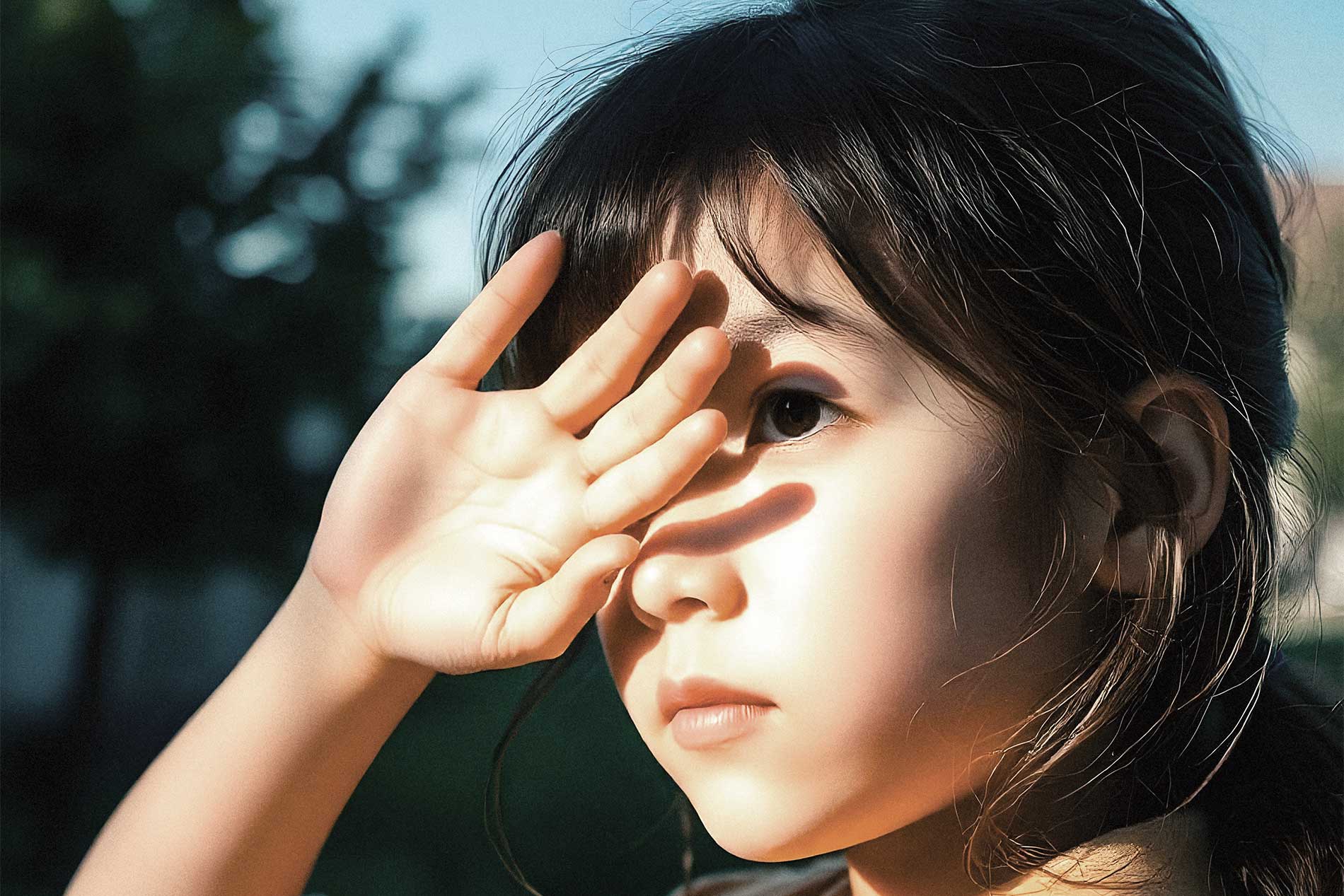 Niña protegiendo sus ojos de la exposición del sol cubriendo su rostro con su mano