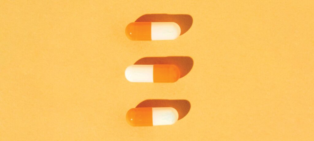 tres cápsulas de medicina alineadas verticalmente sobre fondo anaranjado, representando medicina para el tratamiento del ojo seco