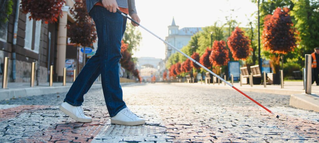 hombre invidente visto de la cintura hacia abajo, cruzando la calle usando un bastón para invidentes