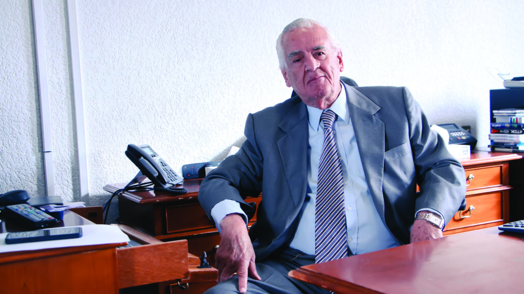 Dr. Rafael Sánchez Fontán, oftalmólogo, en su consultorio, posando para fotografía para entrevista. Se pueden ver artículos de oficina como teléfonos, libros, papeles y otros.