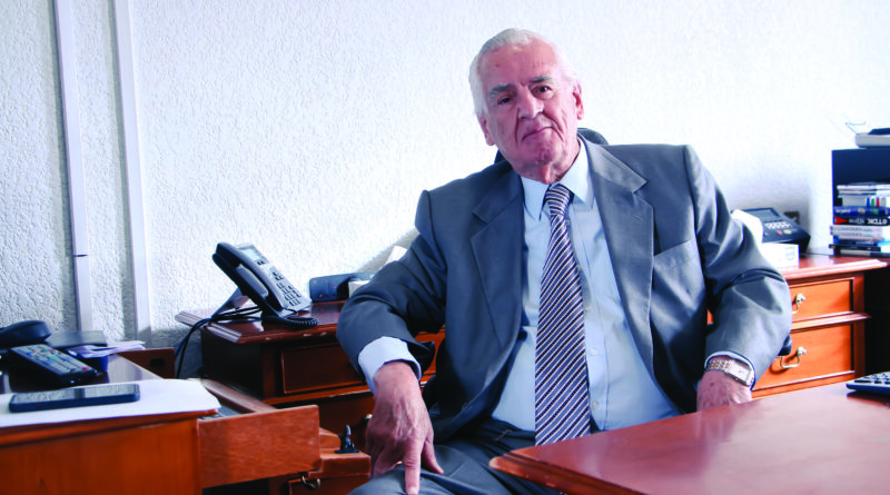 Dr. Rafael Sánchez Fontán, oftalmólogo, en su consultorio, posando para fotografía para entrevista. Se pueden ver artículos de oficina como teléfonos, libros, papeles y otros.