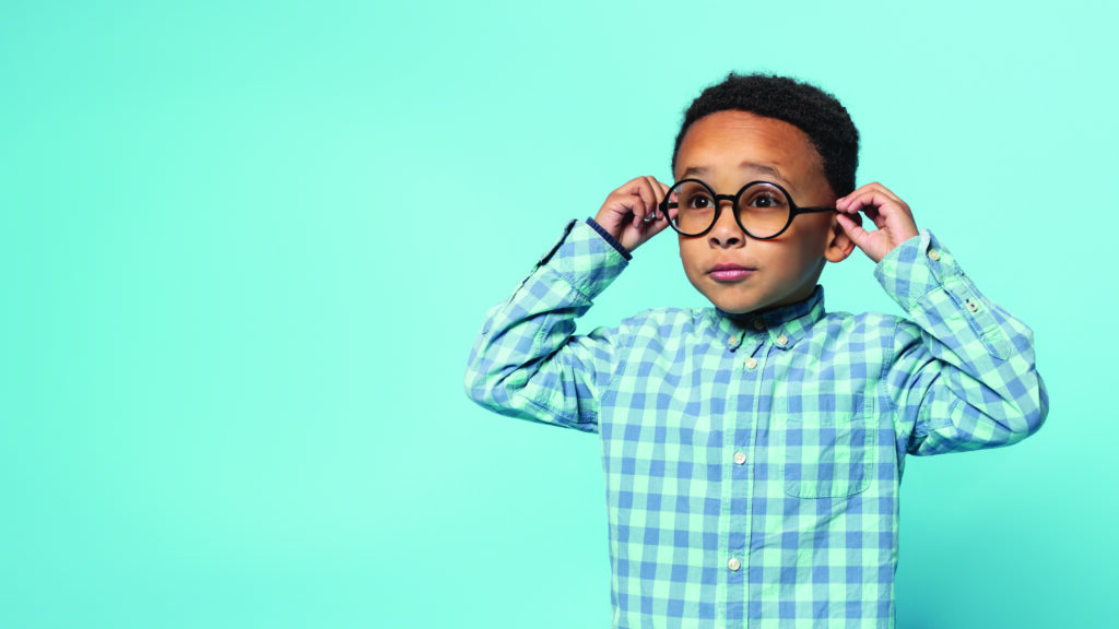 Niño afroamericano con deficiencia visual usando lentes con graduación, posando en un estudio con fondo color azul. En el contexto de los avances en oftalmología con una visión global